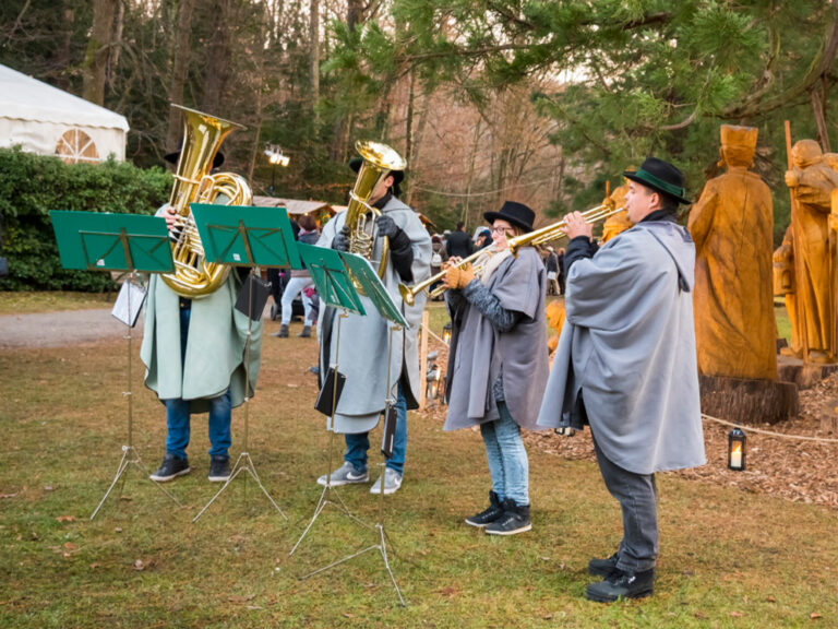 Bläsergruppe in grauen Ponchos spielt Weihnachtsmusik beim Advent im Kurpark Bad Gleichenberg in der Steiermark.